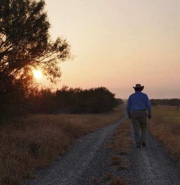 Man walking away down a dirt road at sunset with orange sky